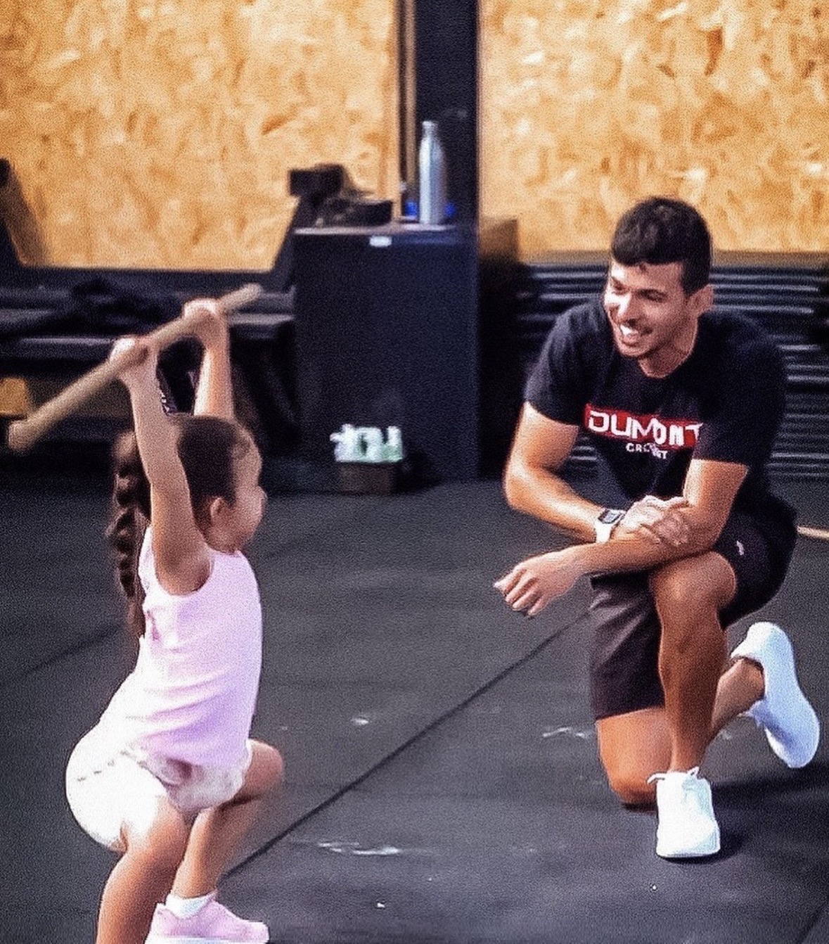 Paulo Mateus orientando uma criança em um exercício de agachamento com bastão